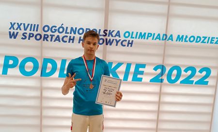 uczeń, w ręku trzyma dyplom, na szyi ma medal, w tle napis ogólnopolska olimpiada młodzieży