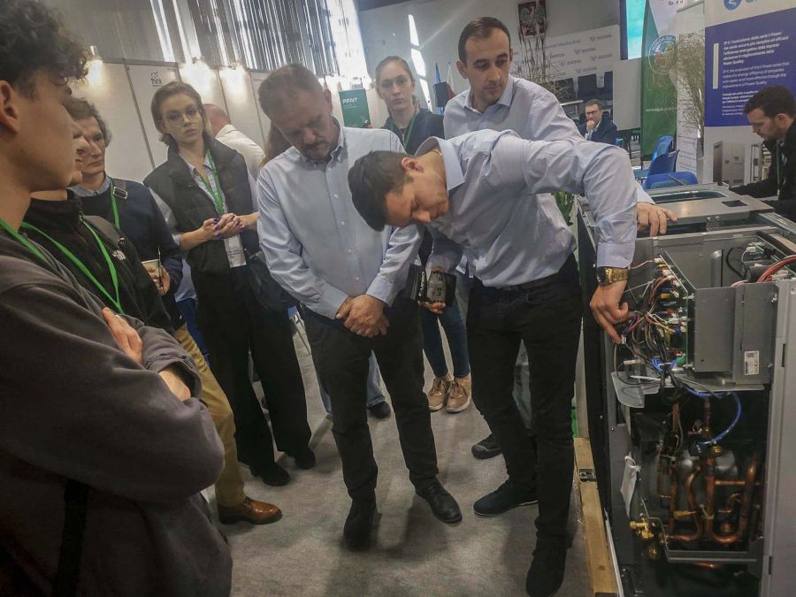 Mężczyzna omawia wnętrze pompy ciepła kilka odób obserwuje pokaz