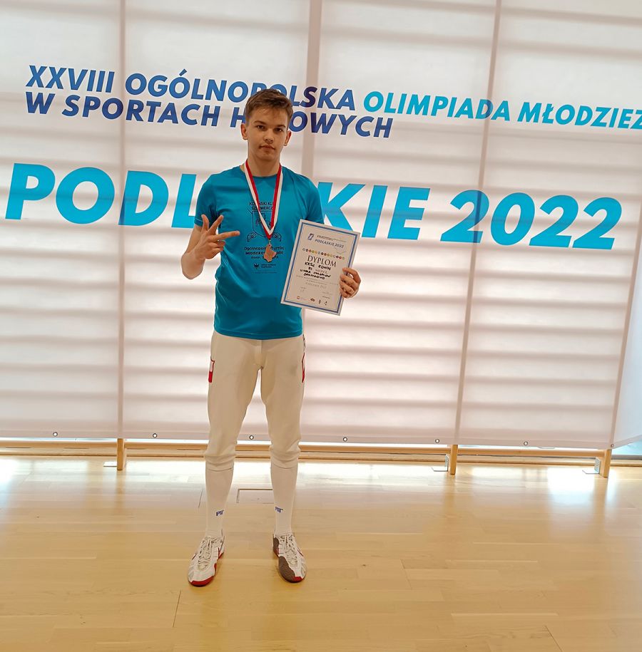 uczeń, w ręku trzyma dyplom, na szyi ma medal, w tle napis ogólnopolska olimpiada młodzieży