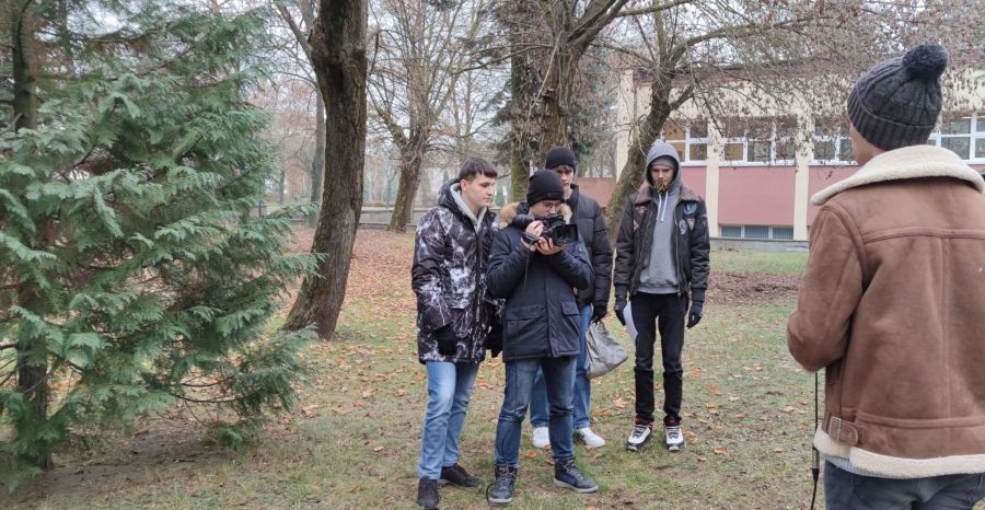 czwórka uczniów, jeden z kamerą, filmują chłopaka stojącego tyłem do kadru