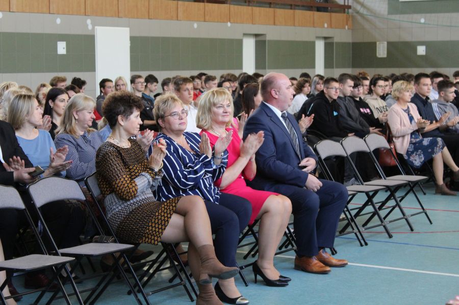 dużo osób siedzi na krzesłach ustawionych w rzędy, na pierwszym planie trzy kobiety i mężczyzna