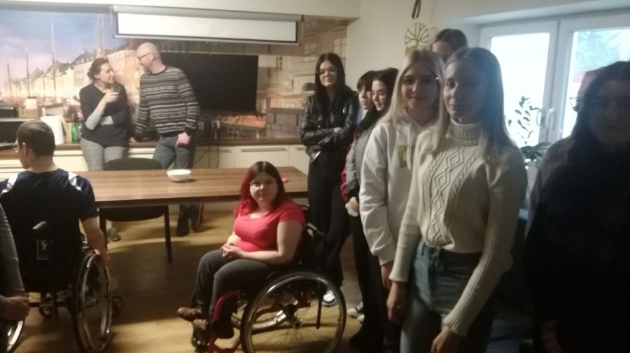 Grupa osób stoi w pomieszczeniu i rozmawia ze sobą. dwie osoby są na wózkach inwalidzkich.