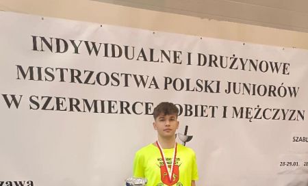 chłopak stoi z pucharem i dyplomem, na szyi ma medal