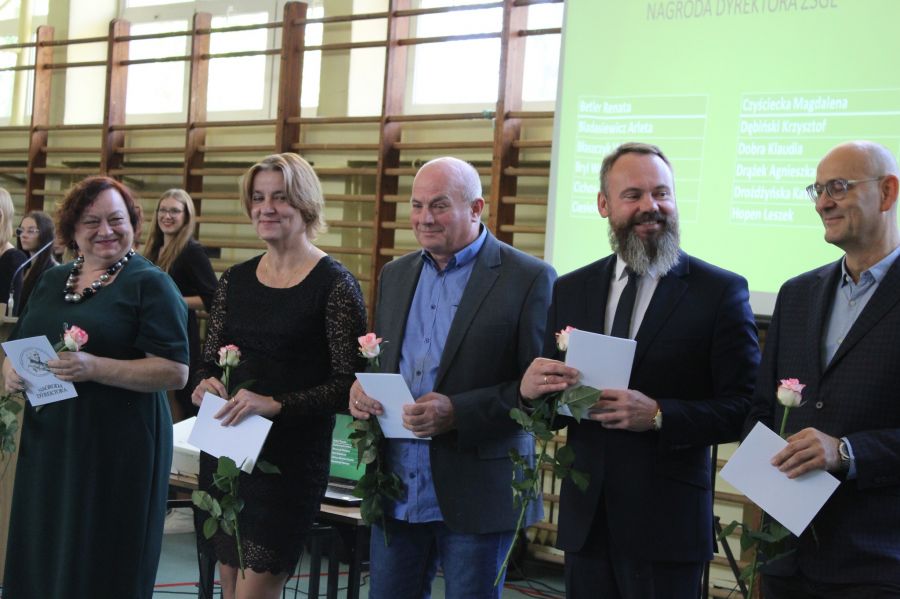 dwie kobiety i trzech mężczyzn stoja obok siebie są uśmiechnięci i trzymają różę oraz białą kartkę