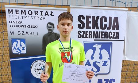 chłopak stoi przodem w rękach trzyma puchar i dyplom na szyi ma medal