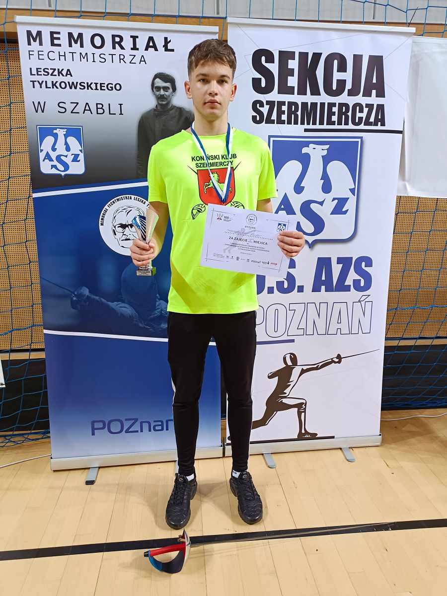 chłopak stoi przodem w rękach trzyma puchar i dyplom na szyi ma medal
