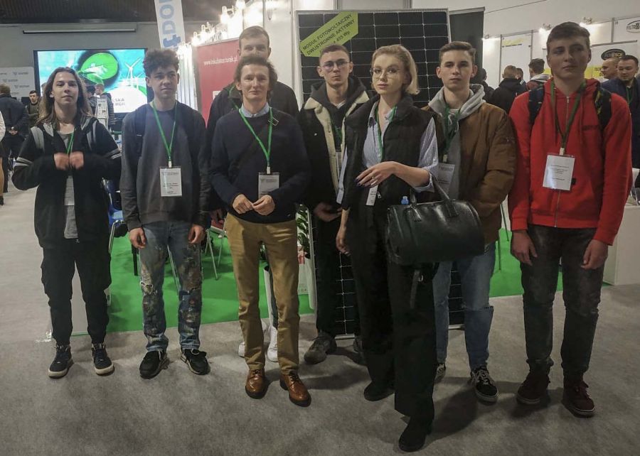 Grupa uczniów i nauczyciel stoją na tle modułów fotowoltaicznych