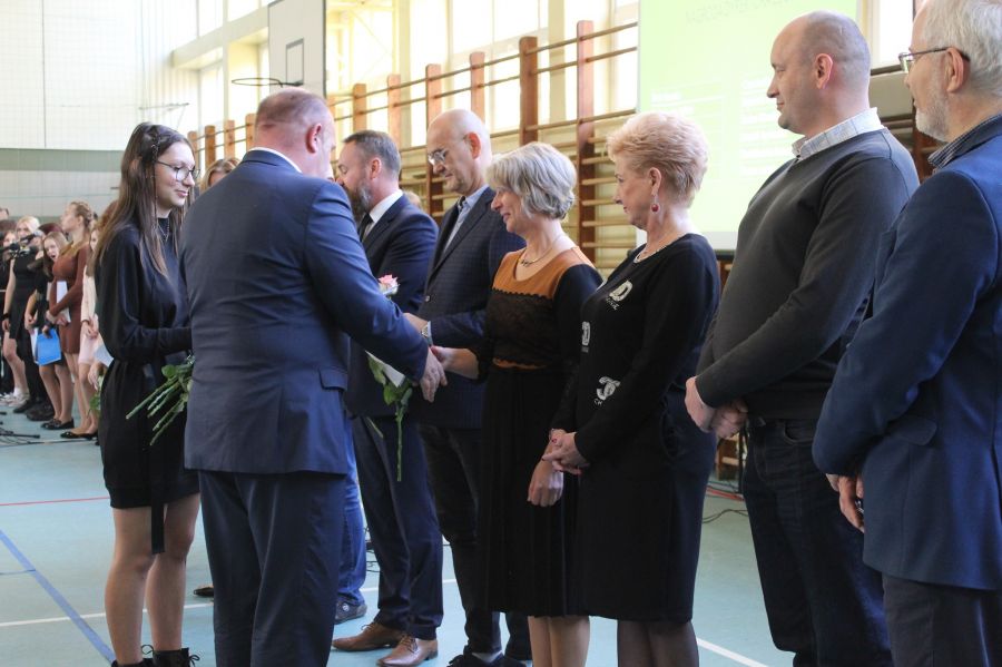 osiem osób, sześć stoi przodem obok siebie jeden z mężczyzn gratuluje kobiecie