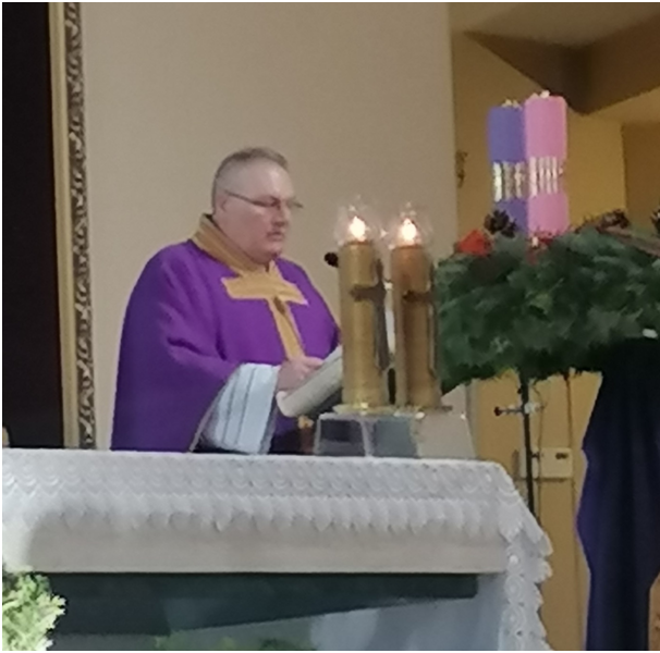 Na zdjęciu ksiądz prałat Zbigniew Cabański  w kościele, przy ołtarzu, podczas odprawianej  dnia 4 grudnia Mszy Świętej w intencji społeczności  Zespołu Szkół Górniczo – Energetycznych w Koninie. Na ołtarzu dwie zapalone świece, obok stoi wieniec adwentowy z widocznymi tylko dwiema świecami fioletową i różową