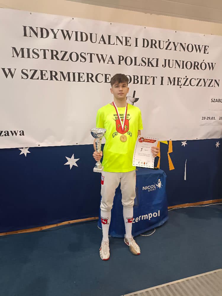 chłopak stoi z pucharem i dyplomem, na szyi ma medal
